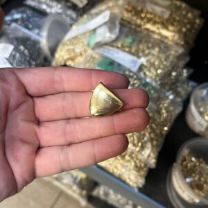Peça dourada em formato triangular arredondado
